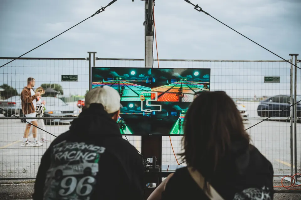 Two people watching a four-way split-screen Mario Kart race