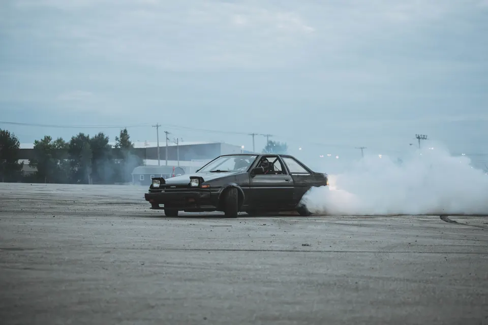 Black Toyota AE86 drifting with a large cloud of tire smoke